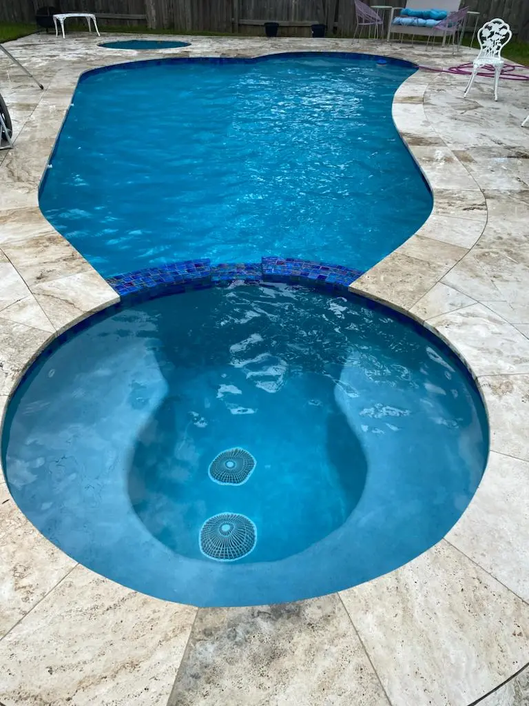 Freeform pool and round spa on travertine deck